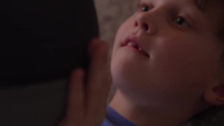 Boy lying down interacts with device in home setting