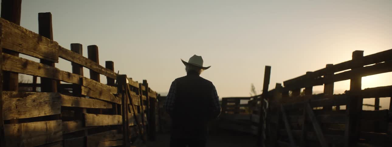 An elderly cowboy walks by wood fences