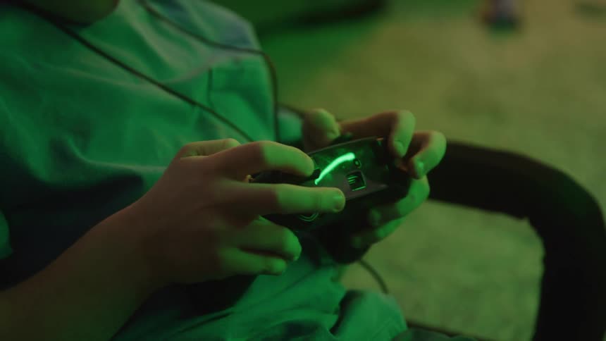 Person holding video game controller plays in room lit by green light