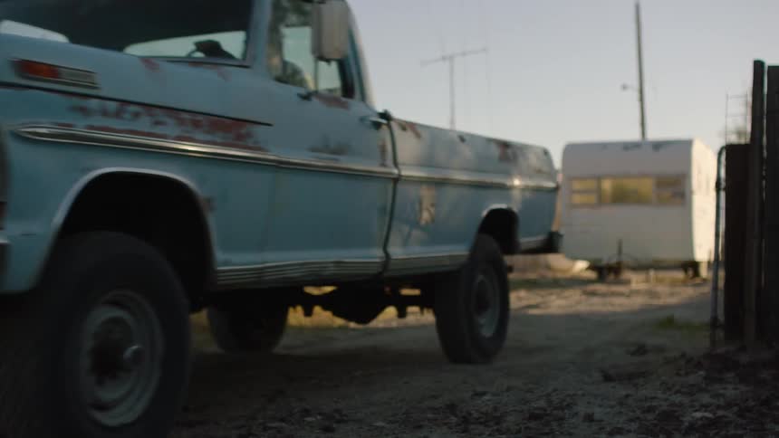 A blue truck drives slowly on a dirt road