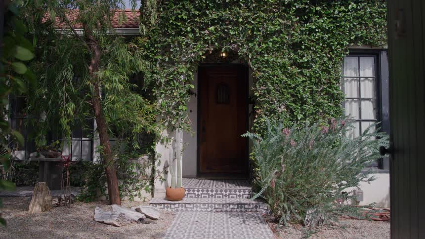 Vinecovered entrance leads to a house surrounded by greenery