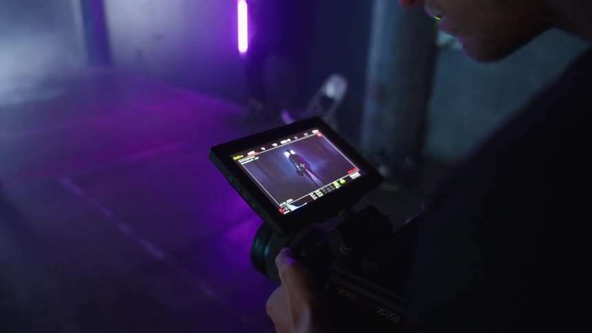 Close up of a male filmmaker viewing media content on a camera screen while on set