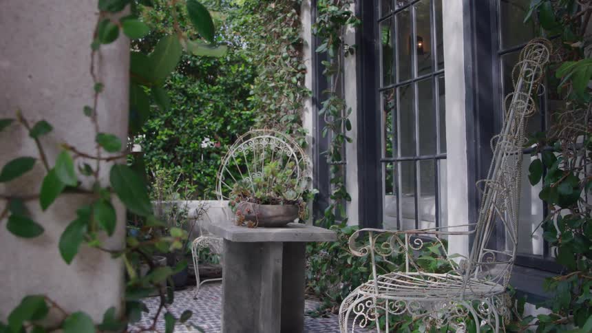 The video is an extreme closeup of a delicate wroughtiron garden chair with a decorative scrollwork design it is positioned outdoors on a stone patio next to a window and ivycovered wall