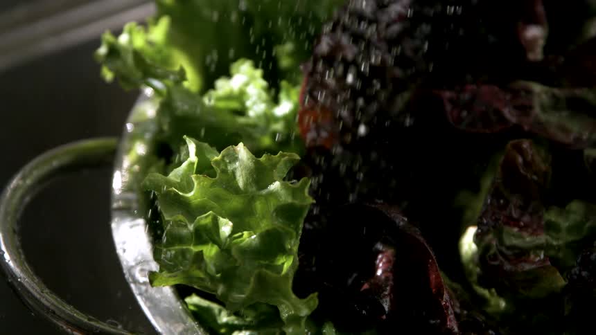 Fresh lettuce leaves are being rinsed with water in a metal colander