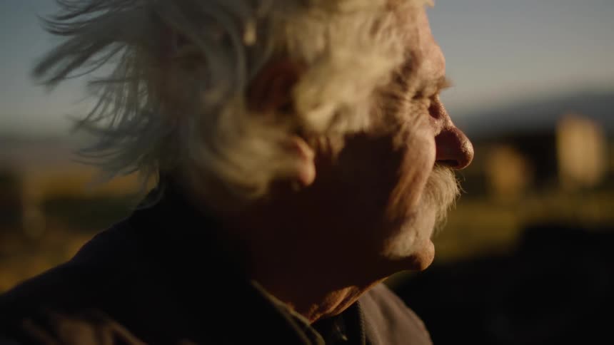 Older man standing outside on windy day looking back and forth