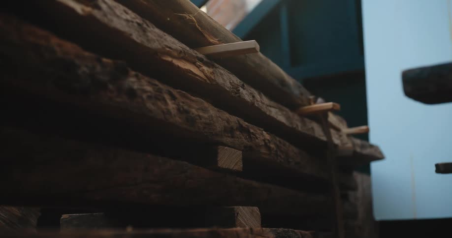 The video is a closeup of a stack of roughhewn dark wood planks the planks are resting on smaller wooden blocks inside what appears to be a shed or storage area