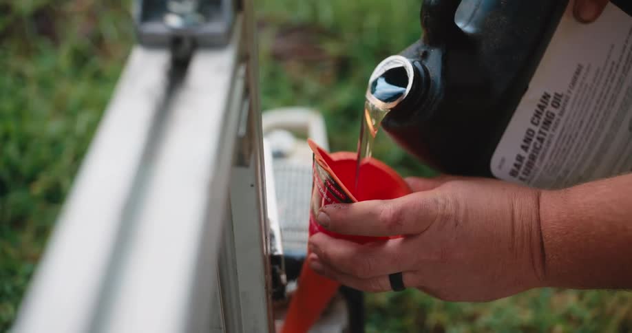 Man adds oil to a machine using a funnel while standing on the lawn