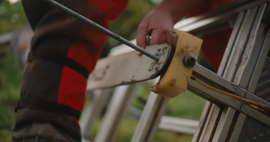 Man tightens a bolt at the end of a chainsaw bar fixed to a metal frame