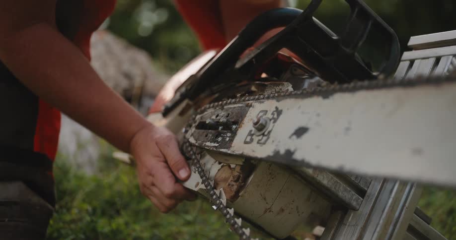 The video is a closeup of a persons hands holding a white and black chainsaw the person is wearing a bright orange shirt and appears to be inspecting or adjusting the tool outdoors in a grassy area