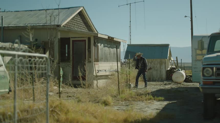A man walks towards a home holding a rifle