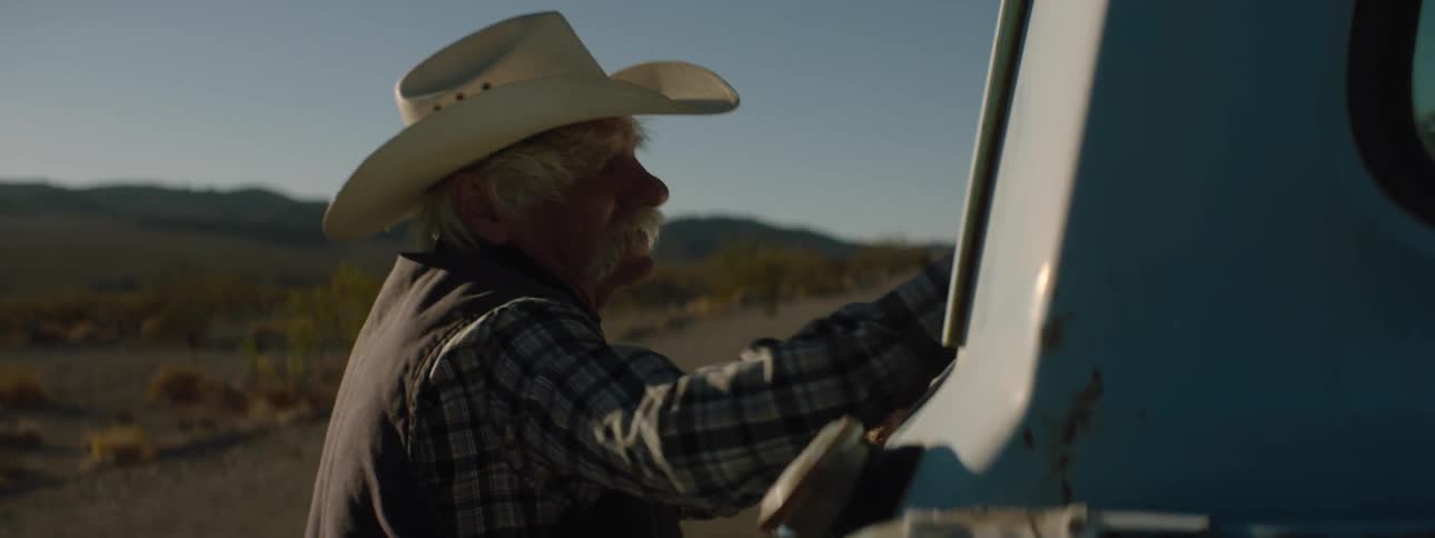 An old cowboy hits the window of a pickup truck with his hand and opens the door