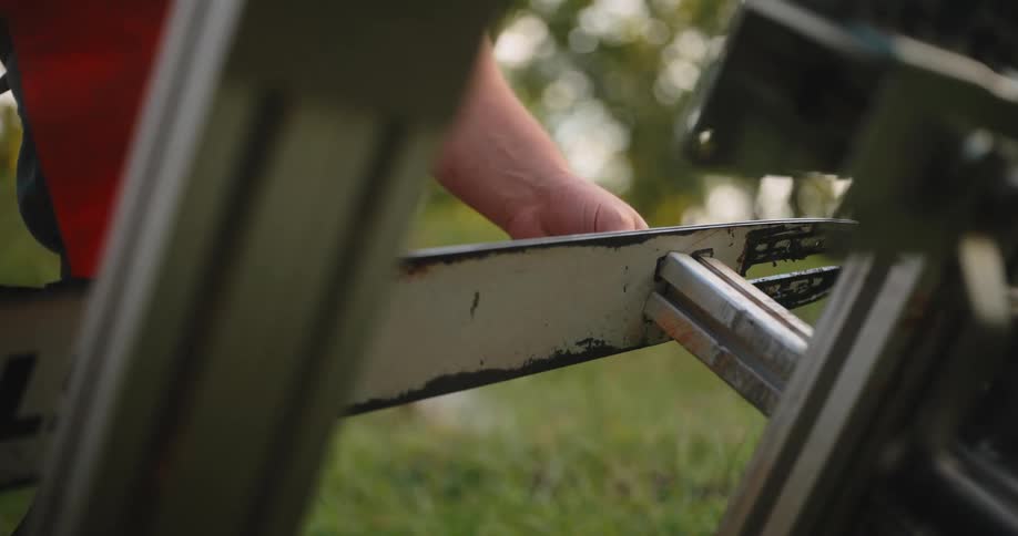 Man tightens a bolt on a metal chainsaw frame resting on the grass
