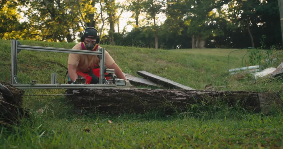 Worker cuts a log with a chainsaw in a grassy outdoor area
