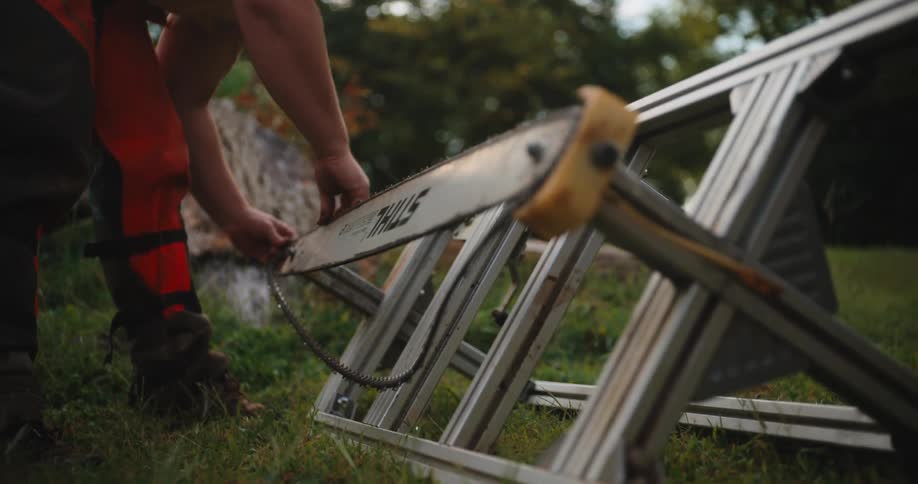Man adjusts the chainsaw chain mounted on a metal frame outdoors