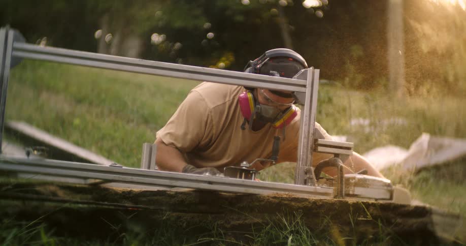 Male woodworker uses a machine while outside in a field on a sunny day