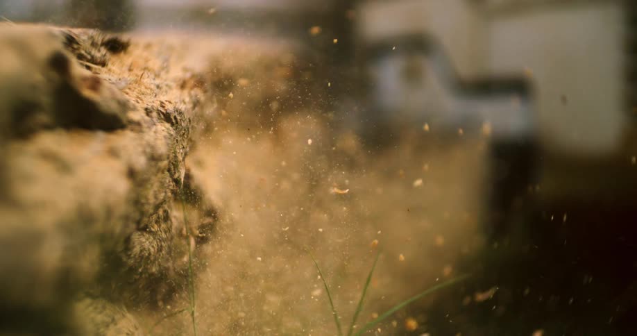 An extremely close slow motion view shows a large quantity of sawdust and wood chips spraying from a cutting log towards the camera lens covering the foreground grass