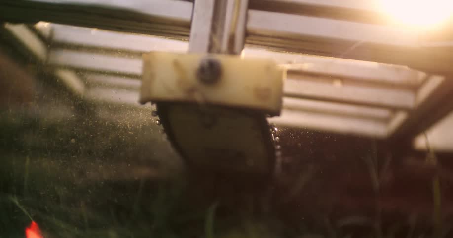 A chainsaw blade moves downward within a metal milling frame cutting a log while throwing a cloud of sawdust into the bright afternoon sun in an extremely close dramatic low angle shot