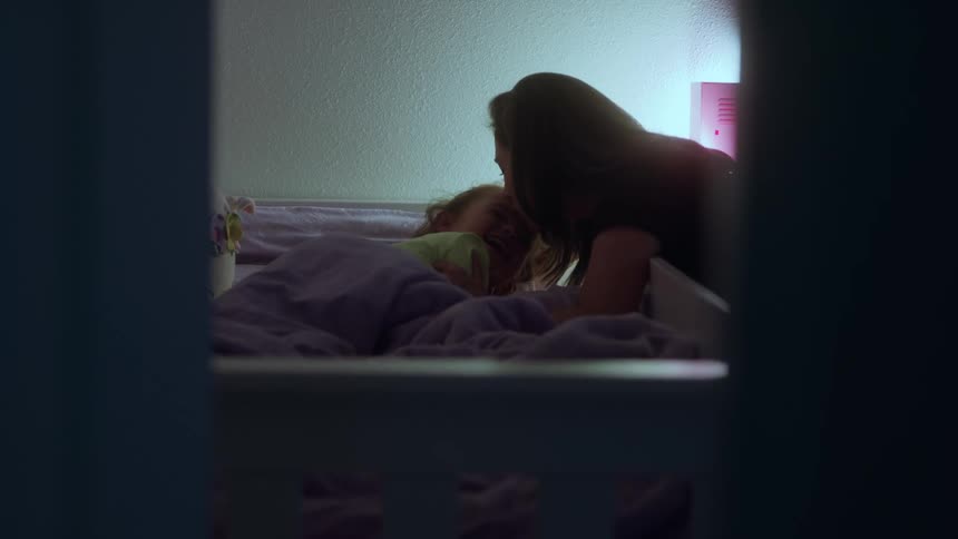 Woman kisses the child lying in bed before sleep