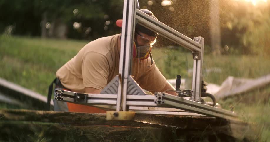 Man wearing protective gear cuts a log with a chainsaw under the evening light