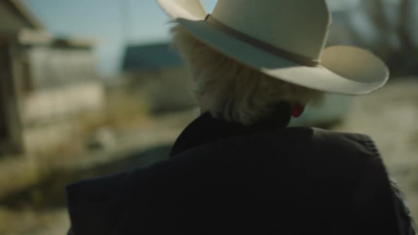 An old cowboy stands outside on a windy day