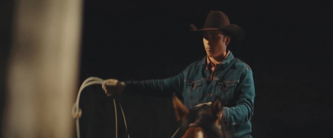 Cowboy rides a horse while spinning a lasso at night