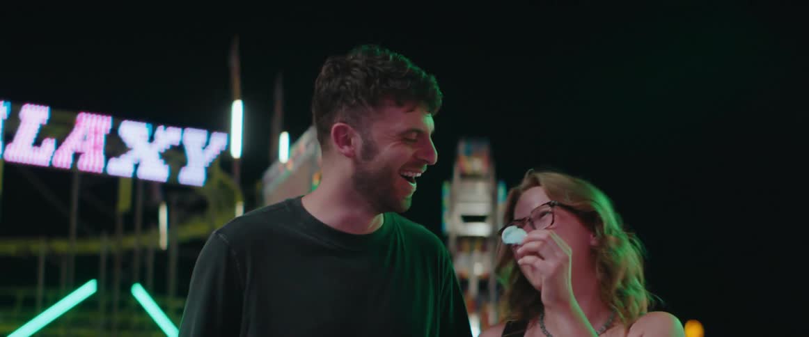 Couple laughs together under colorful lights of a night fair