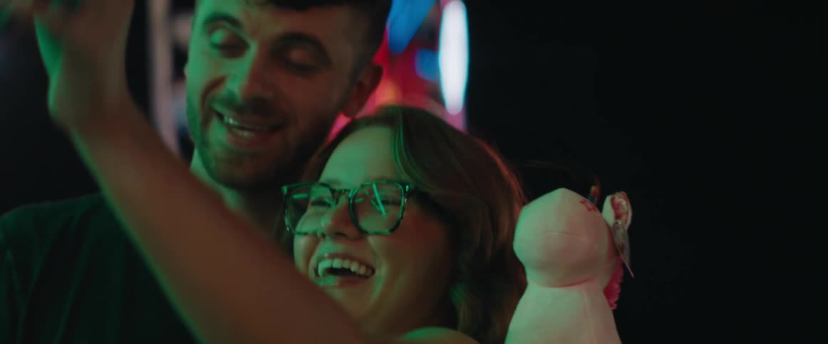 Young man and woman taking a selfie on their smartphone at an amusement park outdoors during night time