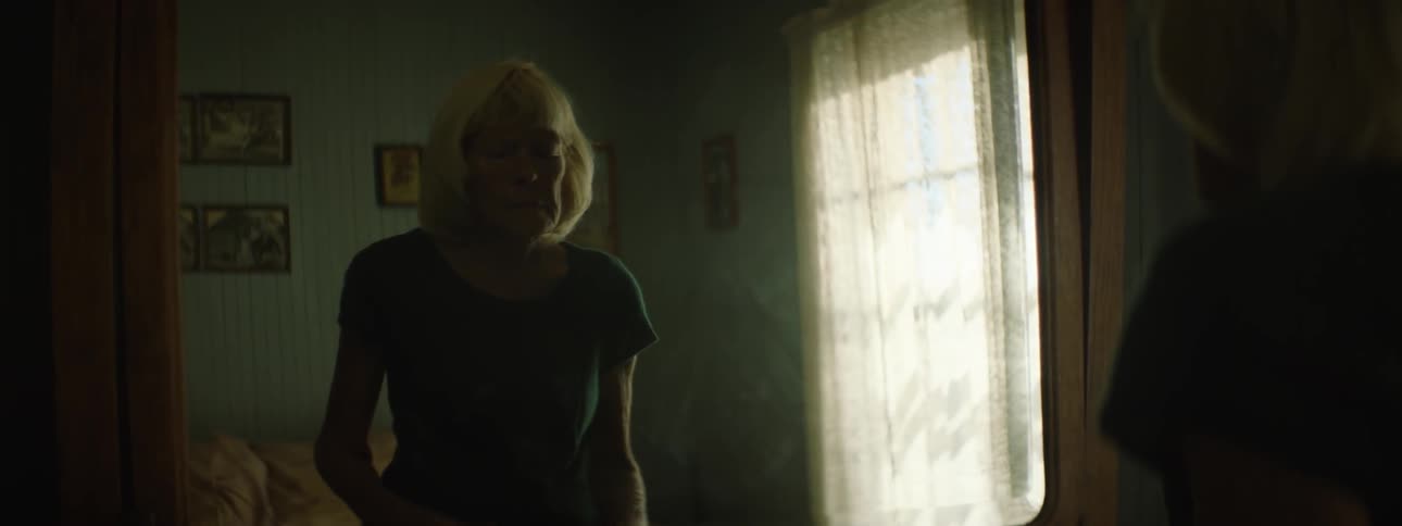 A woman looks in the mirror and adjusts her hair and sweater