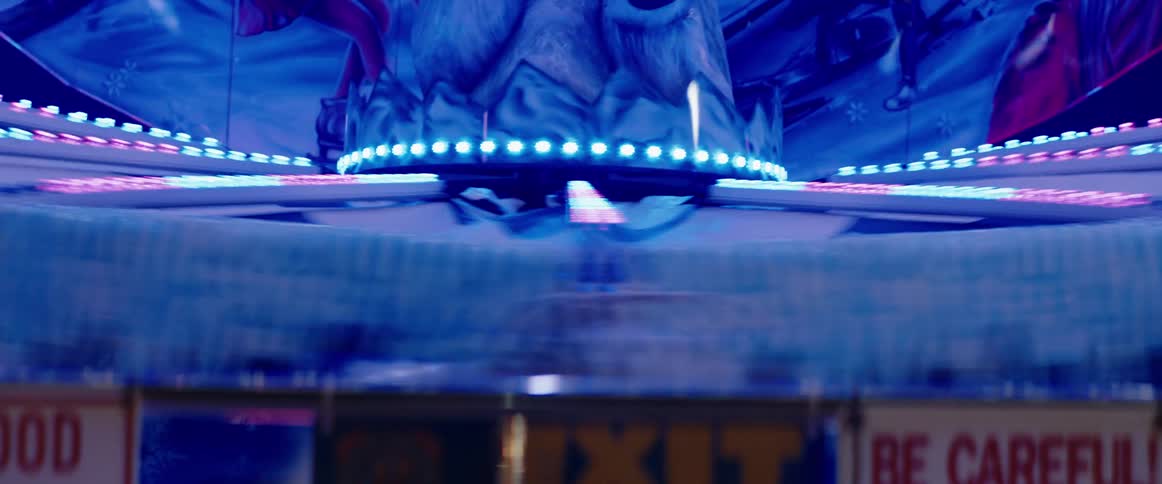 A spinning carnival ride decorated with a blue and white polar bear figure and bright blue neon lights rotates quickly creating a blurring motion effect