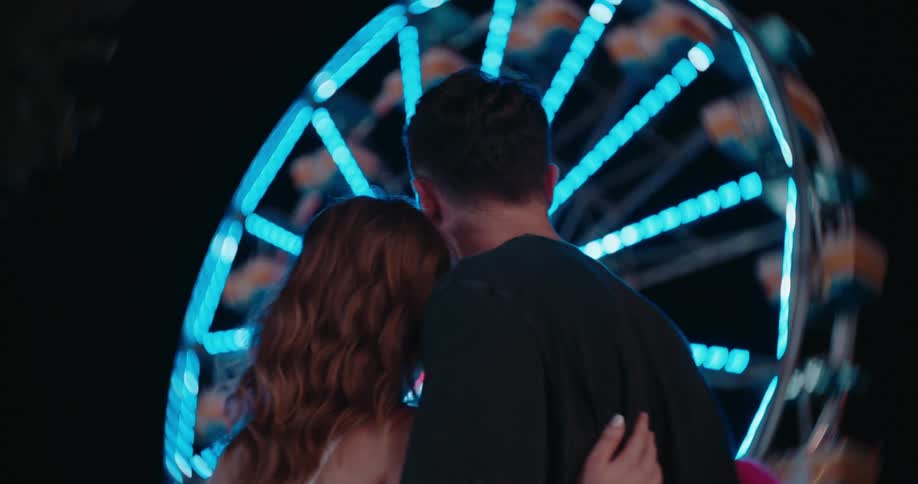 The couple kiss while looking at the ferris wheel