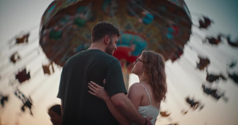 The man and woman smile while looking up at the carnival ride