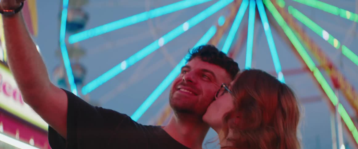Close up of a young adult couple taking a selfie together while standing outdoors in a park