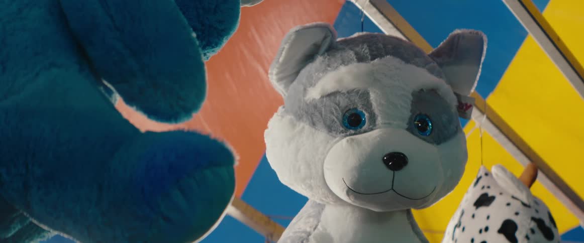 A gray and white stuffed husky dog with glittery blue eyes hanging as a prize at a carnival game stall