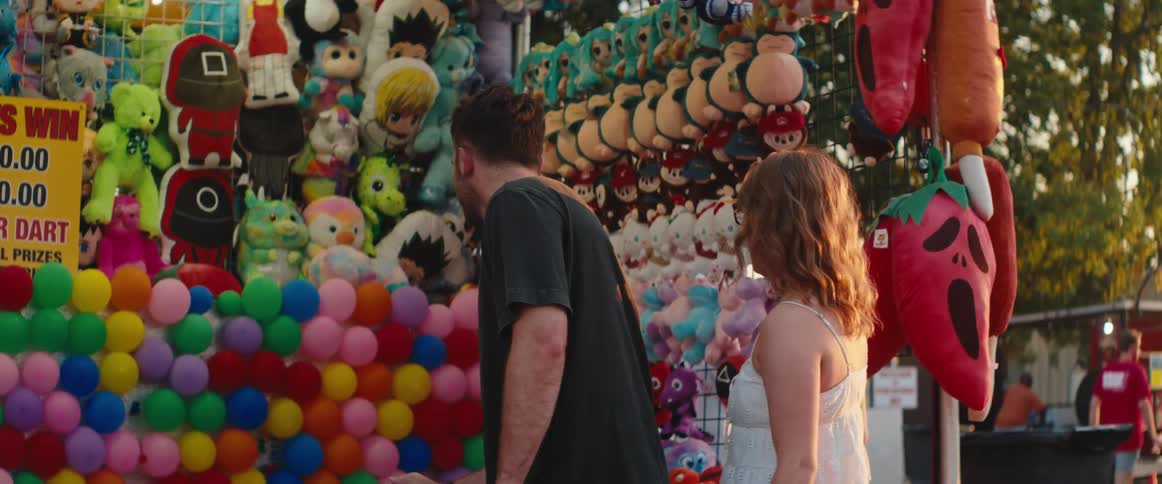 Couple plays a dart game at a booth filled with colorful prizes