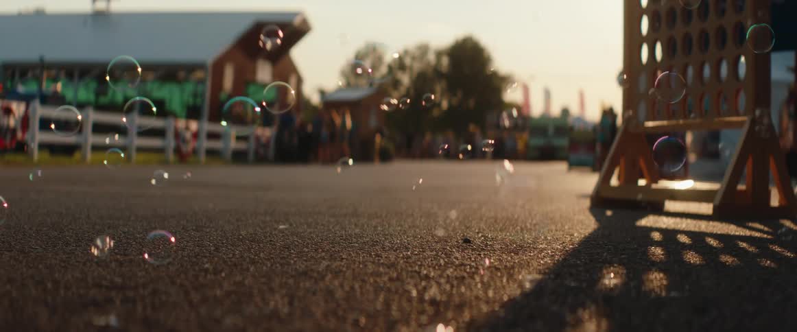 Bubbles float above the asphalt lit by the late afternoon sun