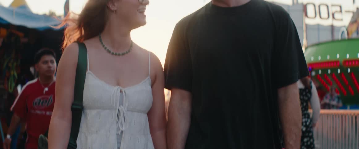 The couple hold hands and talk while walking in the amusement park