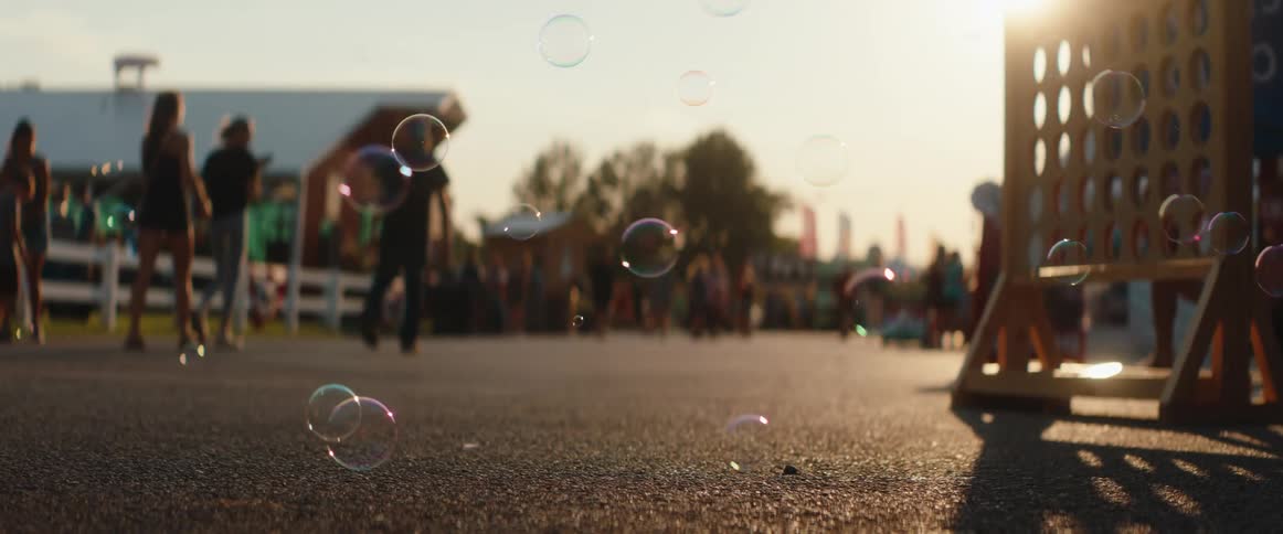People walk among bubbles under the warm evening light