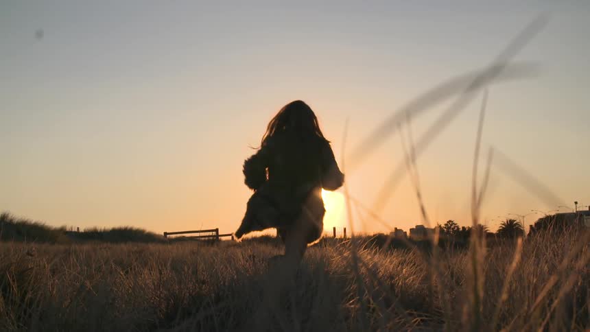 Woman jogging through a grassy field at sunset