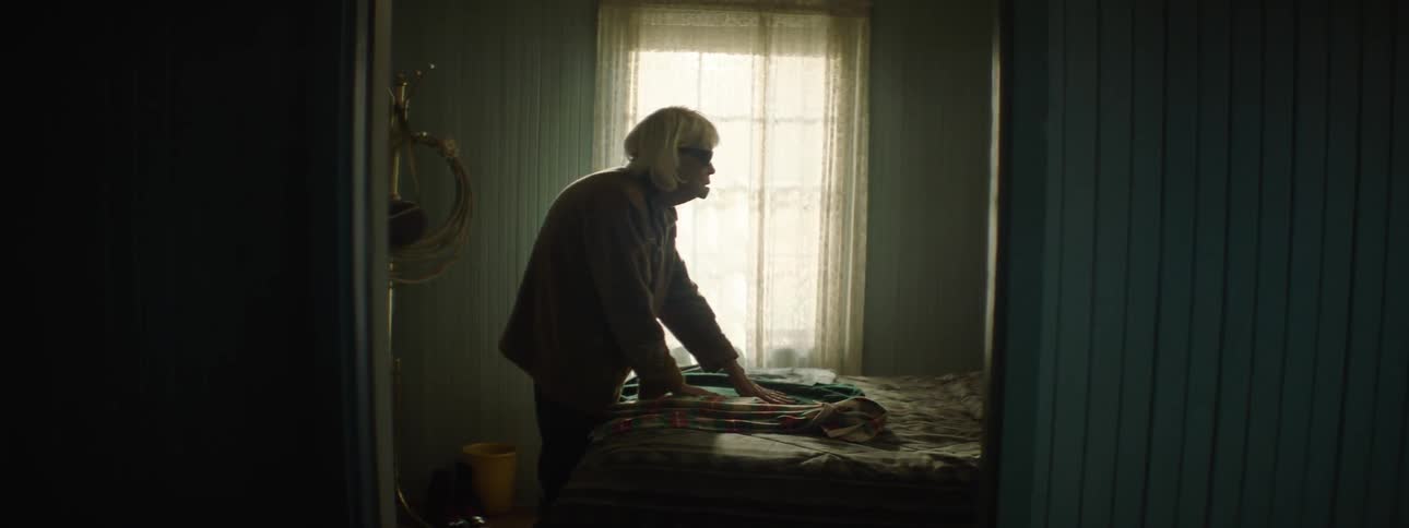 An old, blind woman exams some clothes left on a bed