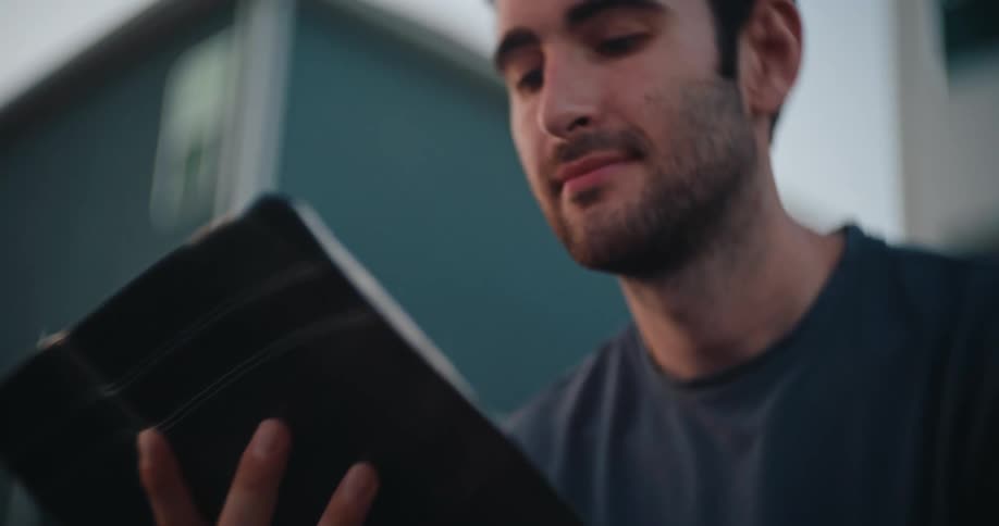 Man reads a book attentively while sitting outdoors