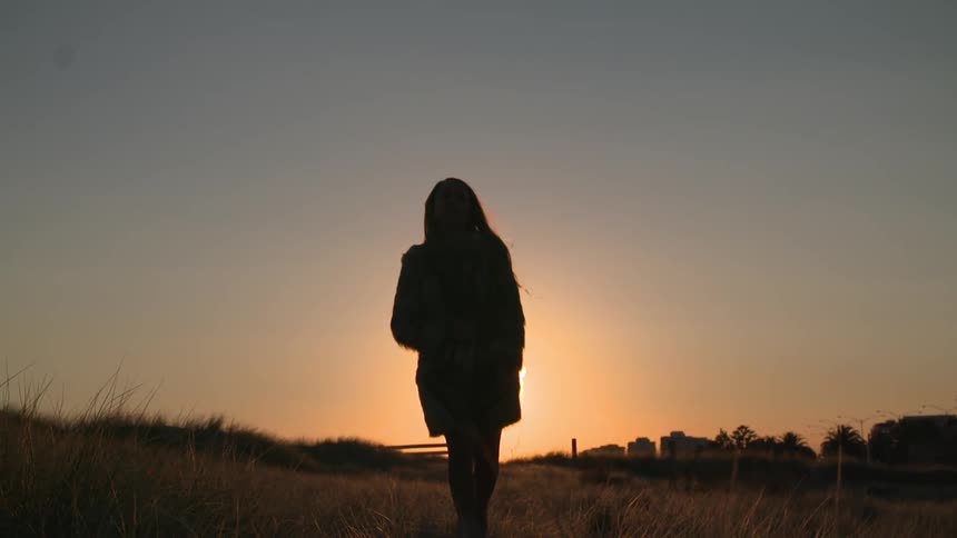 Woman walking through a field at sunset