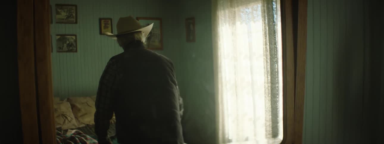 A man wearing a cowboy hat folds clothes and lays them on the bed