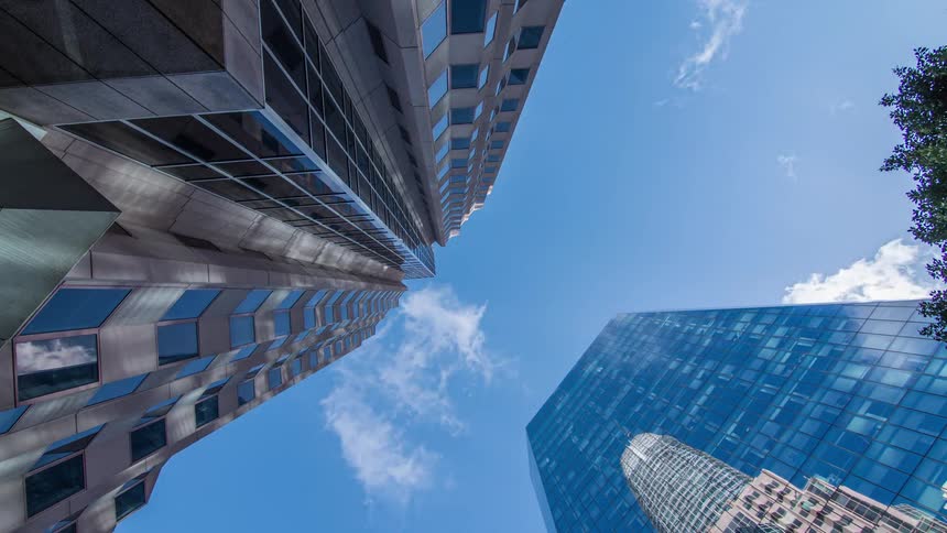 Two skyscrapers rise toward a bright blue sky with scattered cloud