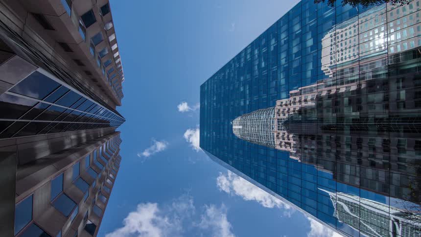 Two large buildings with glass facades on a day with a blue sky and white clouds passing quickly