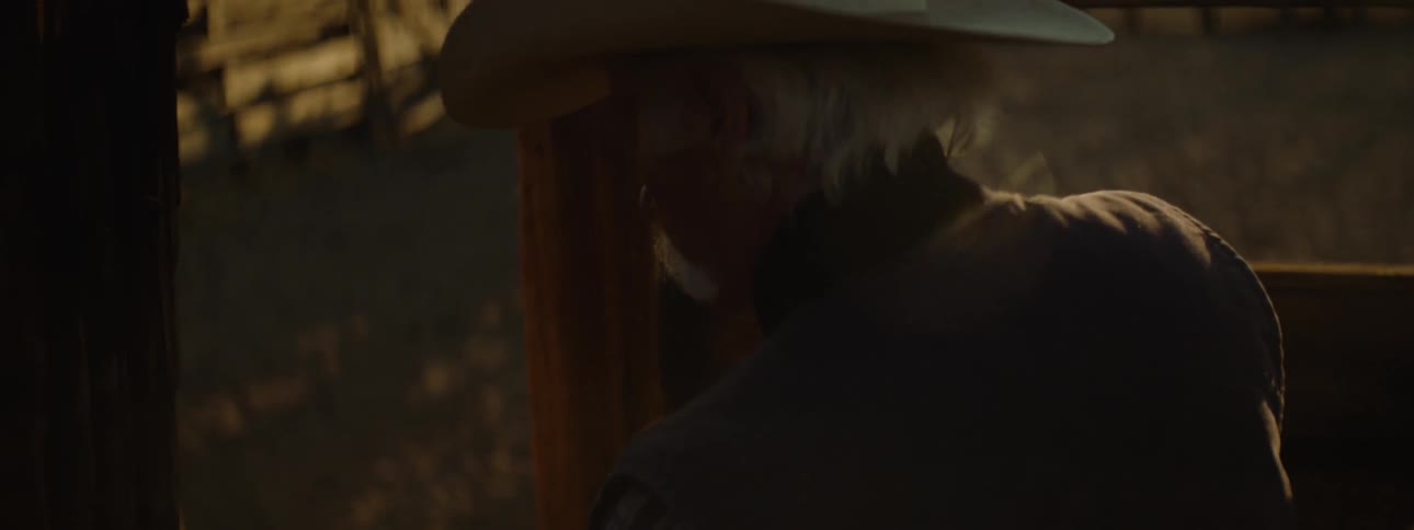 A man in a cowboy hat opens the wooden paddock gate