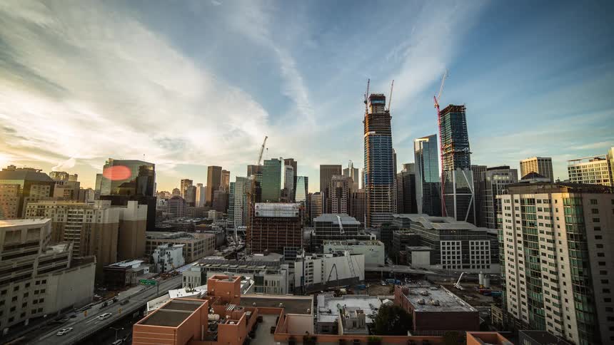 Cranes and skyscrapers dominate the skyline of a city as it grows dark