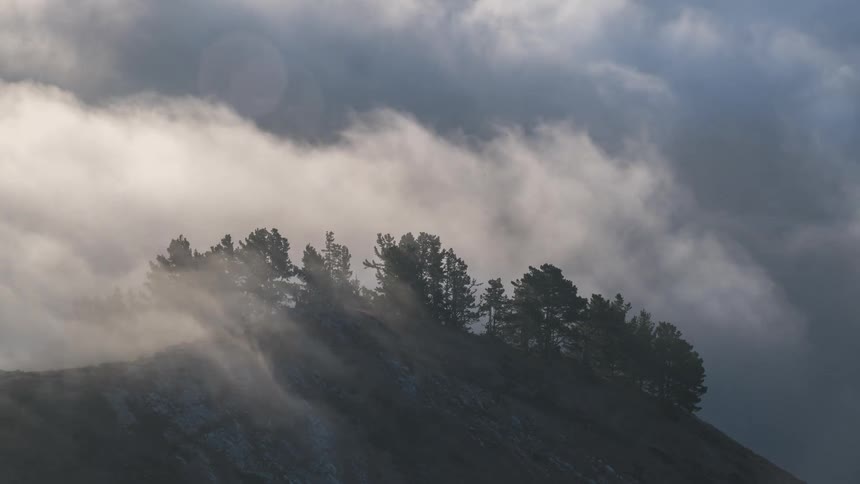 Dark hill with a tree line hidden in thick flowing fog