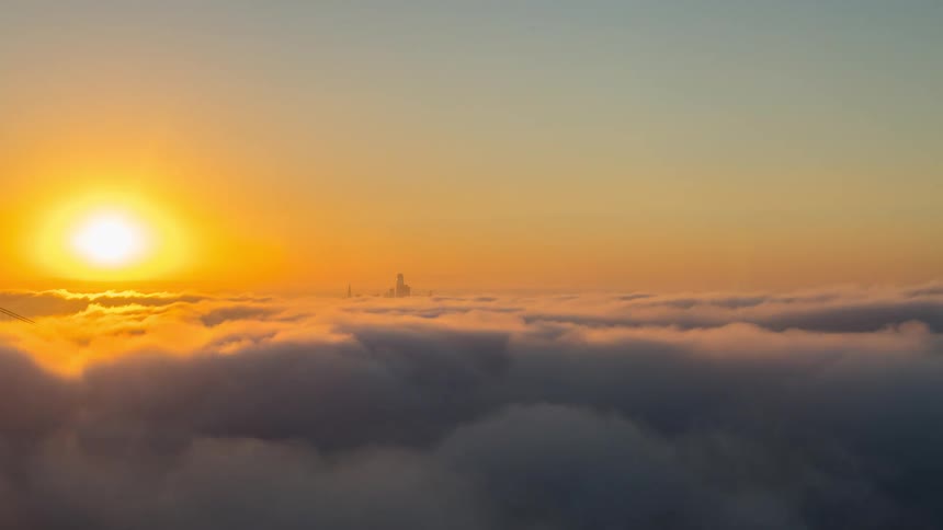 The sun sets over a rolling sea of clouds in this timelapse revealing the tops of distant skyscrapers poking through the fog