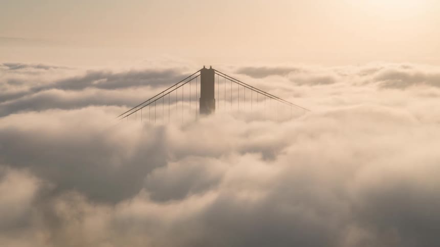 Bridge tower emerges through dense clouds under the soft morning light