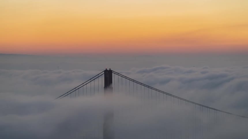 A bridge tower shrouded in fog under a golden orange sunrise